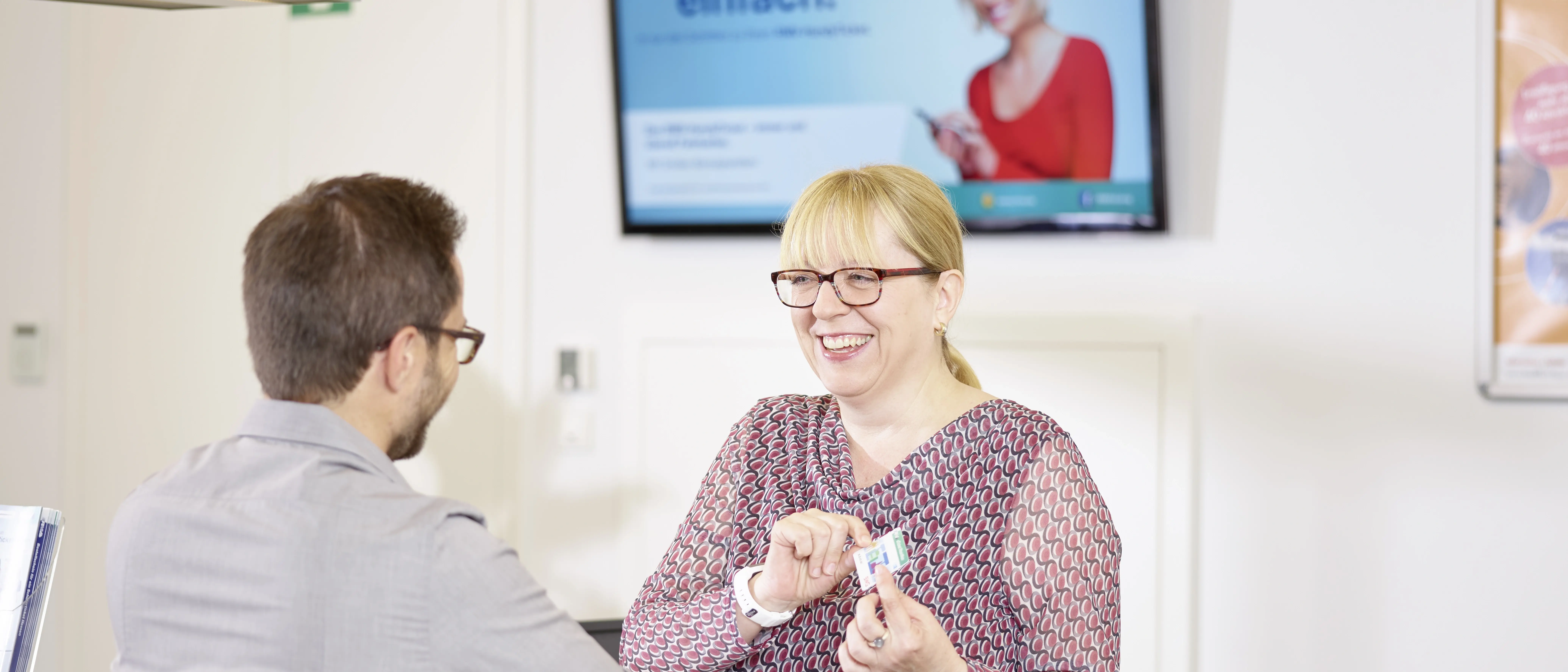 Eine lächelnde Frau berät in der Mobilitätszentrale Gießen einen Mann in Ticketfragen.