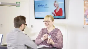 Eine lächelnde Frau berät in der Mobilitätszentrale Gießen einen Mann in Ticketfragen.